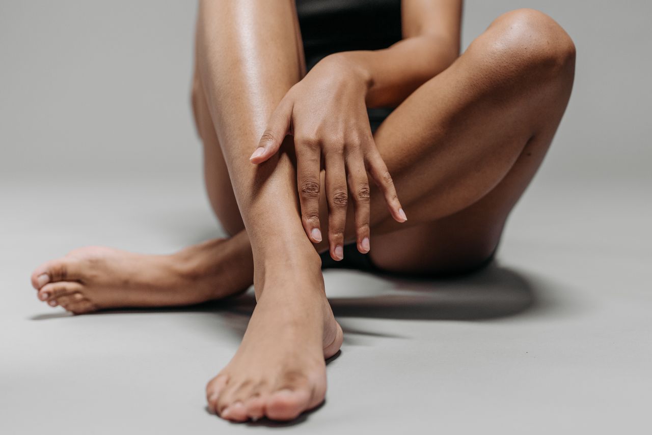 Close-up view of a woman's legs and hands sitting cross-legged on the floor, emphasizing skin tone and texture.